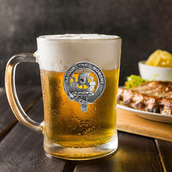 A glass mug filled with beer, featuring a logo, sits on a wooden table next to a plate of food.