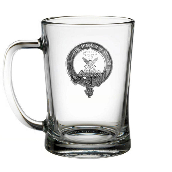 A clear glass mug with a metal emblem featuring a crest and a cross.