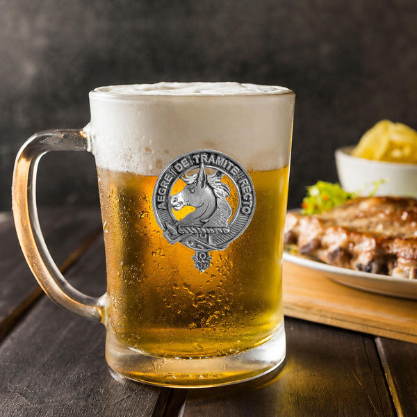 A glass mug filled with beer, featuring a logo, sits on a wooden table next to a plate of food.
