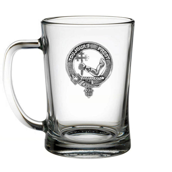 A clear glass mug with a metal emblem featuring a cross and the text "TOUJOUR'S PREST" printed on it.