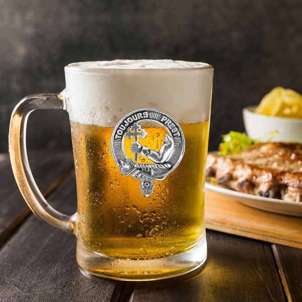 A glass mug filled with beer, featuring a logo, sits on a wooden table next to a plate of food.