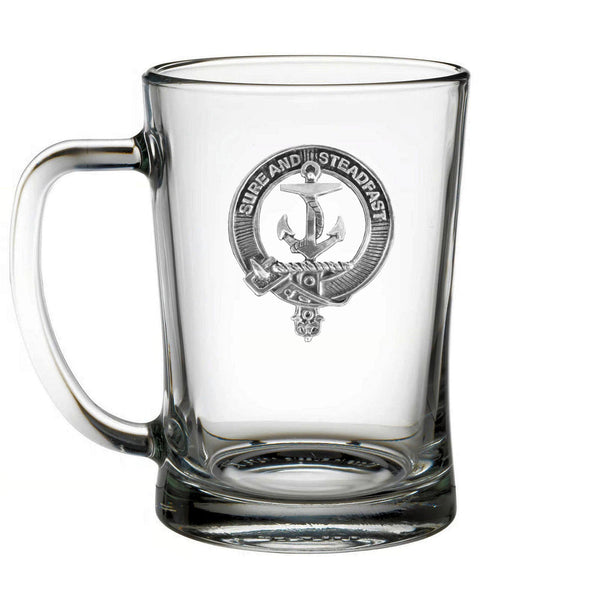 A clear glass mug with a silver emblem featuring an anchor and the text "SURE AND STEADFAST" printed on it.